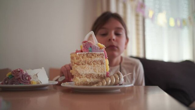 Happy young girl enjoying a large slice of decorative unicorn cake at her birthday party, with a joyful expression