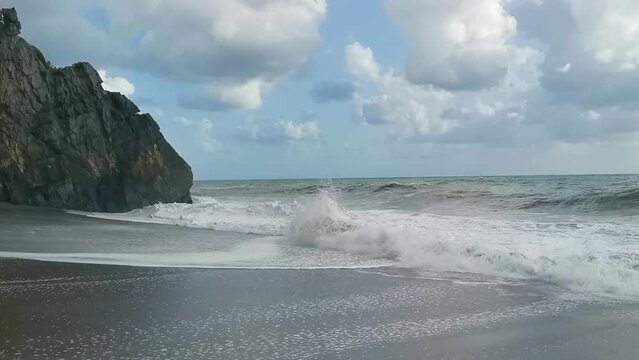 Spiaggia solitaria al rallentatore con il mare agitato: le onde si infrangono sulla roccia e il bagnasciuga
