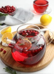 Tasty hot cranberry tea with lemon, rosemary and fresh berries in teapot on white table