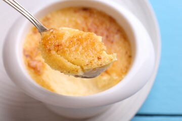 Taking delicious creme brulee with spoon from bowl at light blue table, closeup