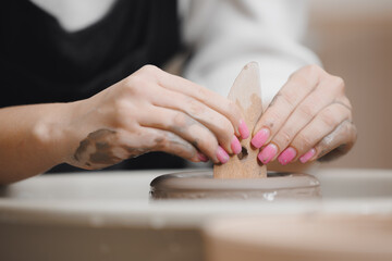 Hands of young girl with manicure master on potter wheel makes clay dishes. Art workshop place for...
