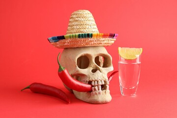 Human scull with Mexican sombrero hat, hot chili peppers and tequila on red background