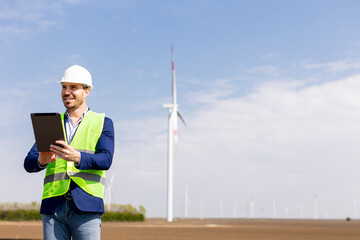 Smiling Engineer With Tablet Inspecting Wind Turbines On A Sunny Day
