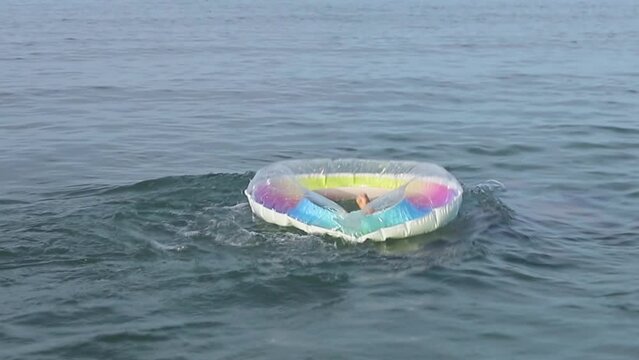 Slow motion teenager jumps and dives inside oa an inflatable swim lap in the sea water