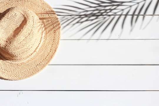 Summertime, vacation, travel, tourism concept. Summer straw hat and shadow of palm leaves on white wooden background. Top view, space for text.