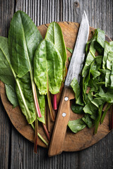 Cutting fresh organic sorrel leaves on wooden board with knife close up. Food photography