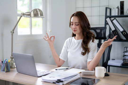 Businesswoman practicing mindfulness meditation to de-stress and refocus at her home office desk.