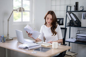 A young woman concentrated on budgeting with papers and laptop in a home office.