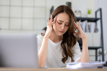 Fototapeta premium A businesswoman appears stressed and experiencing a headache while focusing on her work in home office.