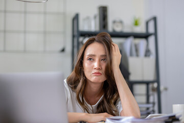 Businesswoman looks stressed, bored and holding her head. Indicates a headache while working at a...