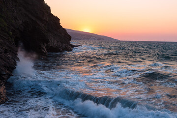 Scenic view to the costal town of Evdilos with rough sea and rocky coast at sunset.