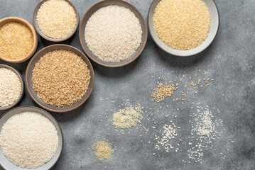 Different varieties of uncooked rice in bowls on a gray background, corner frame. Top view, flat lay, copy space. - 767278263