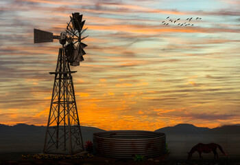Windmill against the setting sun on a farm or ranch.