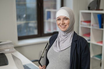 Pregnant Caucasian woman in hijab working in the office. 