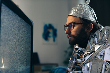 Conspiracy Theory on Screen: Man in Tin Foil Hat and Blanket Observing TV Interference
