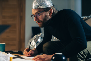 Unveiling Conspiracies: Man in Foil Hat Crafting Cryptic Signs - obrazy, fototapety, plakaty