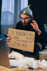 A conspiracy theorist in a tinfoil hat holds a sign in his hands.