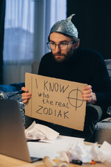 A conspiracy theorist in a tinfoil hat holds a sign in his hands.