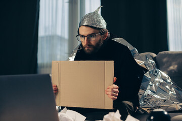 A conspiracy theorist in a tinfoil hat holds a sign in his hands. - obrazy, fototapety, plakaty