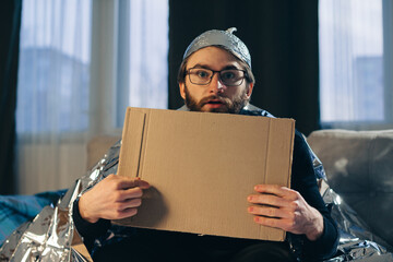 A conspiracy theorist in a tinfoil hat holds a sign board in his hands.