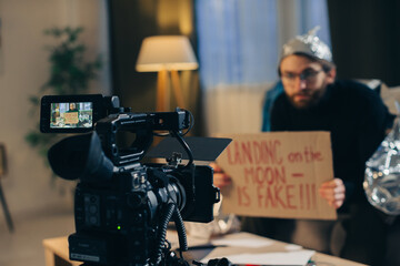 A conspiracy theorist shoots pseudoscientific videos on camera. A man in a tinfoil hat and a sign...