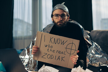 A conspiracy theorist in a tinfoil hat holds a sign in his hands.