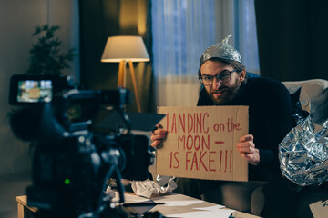 A conspiracy theorist shoots pseudoscientific videos on camera. A man in a tinfoil hat and a sign...