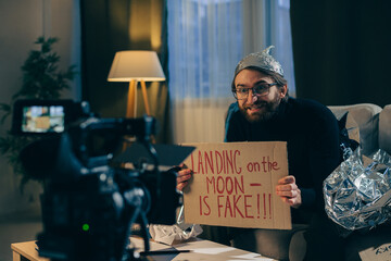 A conspiracy theorist shoots pseudoscientific videos on camera. A man in a tinfoil hat and a sign...