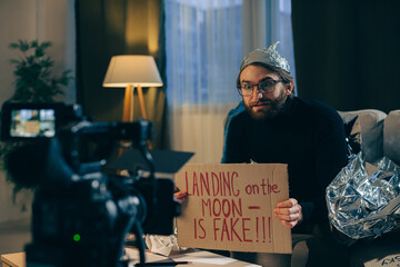 A conspiracy theorist shoots pseudoscientific videos on camera. A man in a tinfoil hat and a sign...