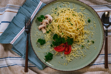 noodles spagetti with butter served with cheese, tomatoes , mushroom and parsley on table cloth, blue napkin, light green ceramic plate