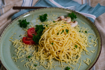 noodles spagetti with butter served with cheese, tomatoes , mushroom and parsley on table cloth, blue napkin, light green ceramic plate