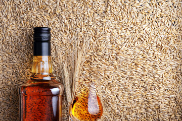 A glass of whiskey with bottle on barley grains as background, top view - 767290294