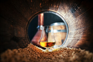 A glass of bourbon whiskey in old oak barrel. Copper alambic and oak barrel on background. Traditional alcohol distillery concept - 767291002