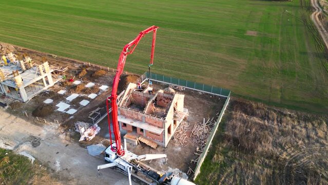 Aerial drone footage of a concrete boom pump truck pouring freshly mixed concrete on a new building. Slab building foundation casting. Cement mix laying on a new residence. Workers at height.
