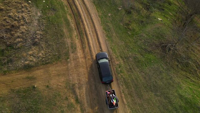 Aerial high angle top down shot of a black car towing a small trailer with two off road cross morotbikes along a windy dirt road. Drone footage of vehicle with a trailer behind going to sports event.
