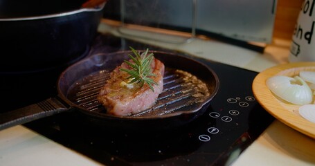 A piece of meat is cooking on a grill with some herbs on top. Concept of warmth and comfort, as it is a common scene in many households where people gather around the kitchen to enjoy a meal together