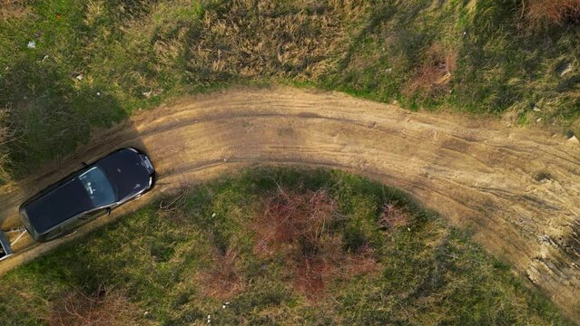 Aerial high angle top down shot of a black car towing a small trailer with two off road cross morotbikes along a windy dirt road. Drone footage of vehicle with a trailer behind going to sports event.
