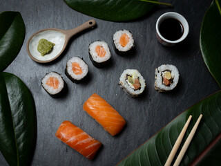 sushi preparado sobre hojas plato y pizarra con fondo negro