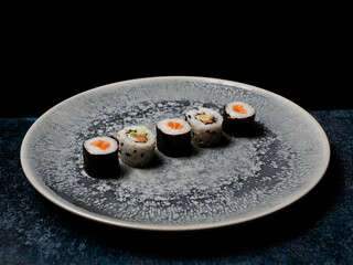 sushi preparado sobre hojas plato y pizarra con fondo negro
