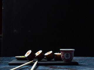 sushi preparado sobre hojas plato y pizarra con fondo negro