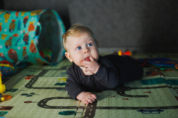 A little 6-month-old boy is learning to crawl on a rug, the child is crawling and holding his head....