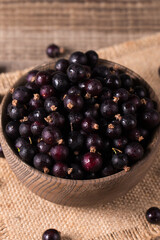 Black currant in a bowl on wooden background. Organic berries. 