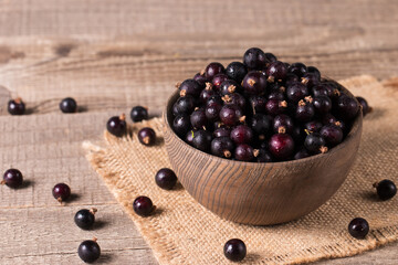 Black currant in a bowl on wooden background. Organic berries. 