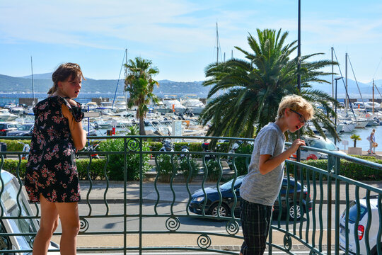 Two children stand on a balcony with an astonished expression on their faces, in the background the harbor with many boats