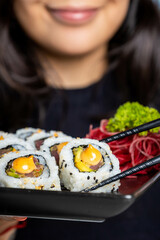 A girl enjoying a delicious tuna and avocado sushi with Sriracha mayo using chopsticks