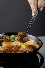 A hand picking up a piece of ramen meat with chopsticks