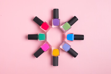 Coloured bright nail polish bottles stacked circle on a pink background
