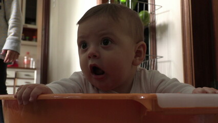 Cute baby infant inside plastic laundry bucket looking up