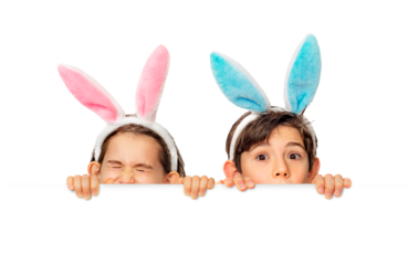 Children hunt for Easter eggs.  A boy and a girl wearing bunny ears peek out curiously from behind a white sheet of paper. 