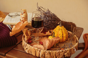 Glass of red wine on wooden table decorated with pumpkins, books and dried leaves outdoor. Autumn...